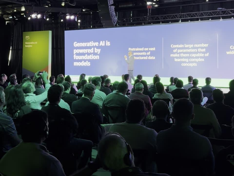 Ritesh Vajariya presenting the foundation-models framework to a large enterprise audience under industrial truss lighting